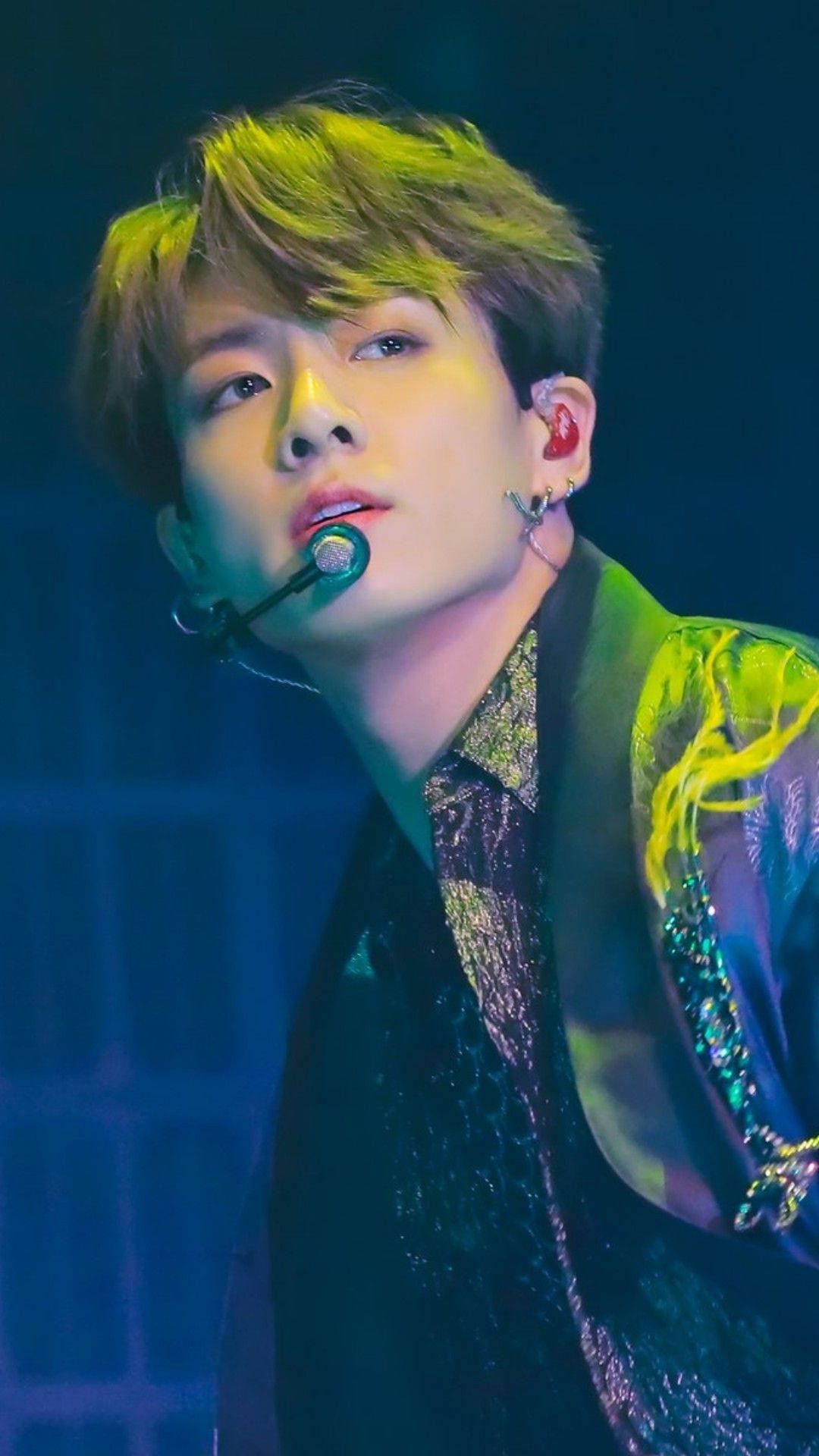 K-pop 表演者在藍色燈光下，以發光的頭髮和閃閃發光的服裝在舞台上唱歌。 — Bts 壁紙