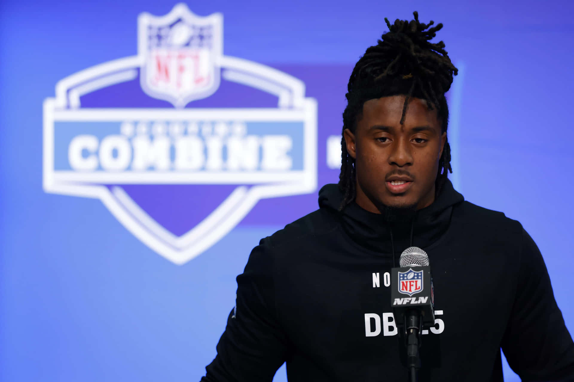  壁紙 — 一位年輕的黑人美式足球員，留著辮子頭，在NFL選秀聯合試訓記者會上對著麥克風說話。