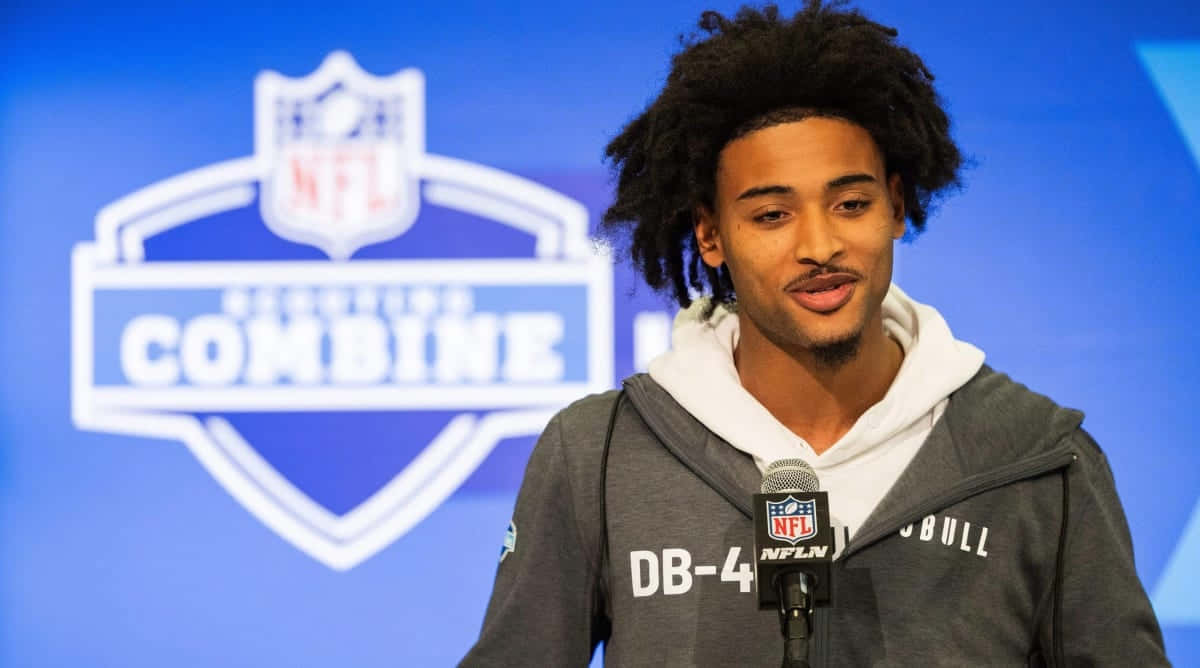  壁紙 — 一位年輕的黑人美式足球員，留著捲髮，在NFL選秀聯合試訓記者會上對著麥克風發言。
