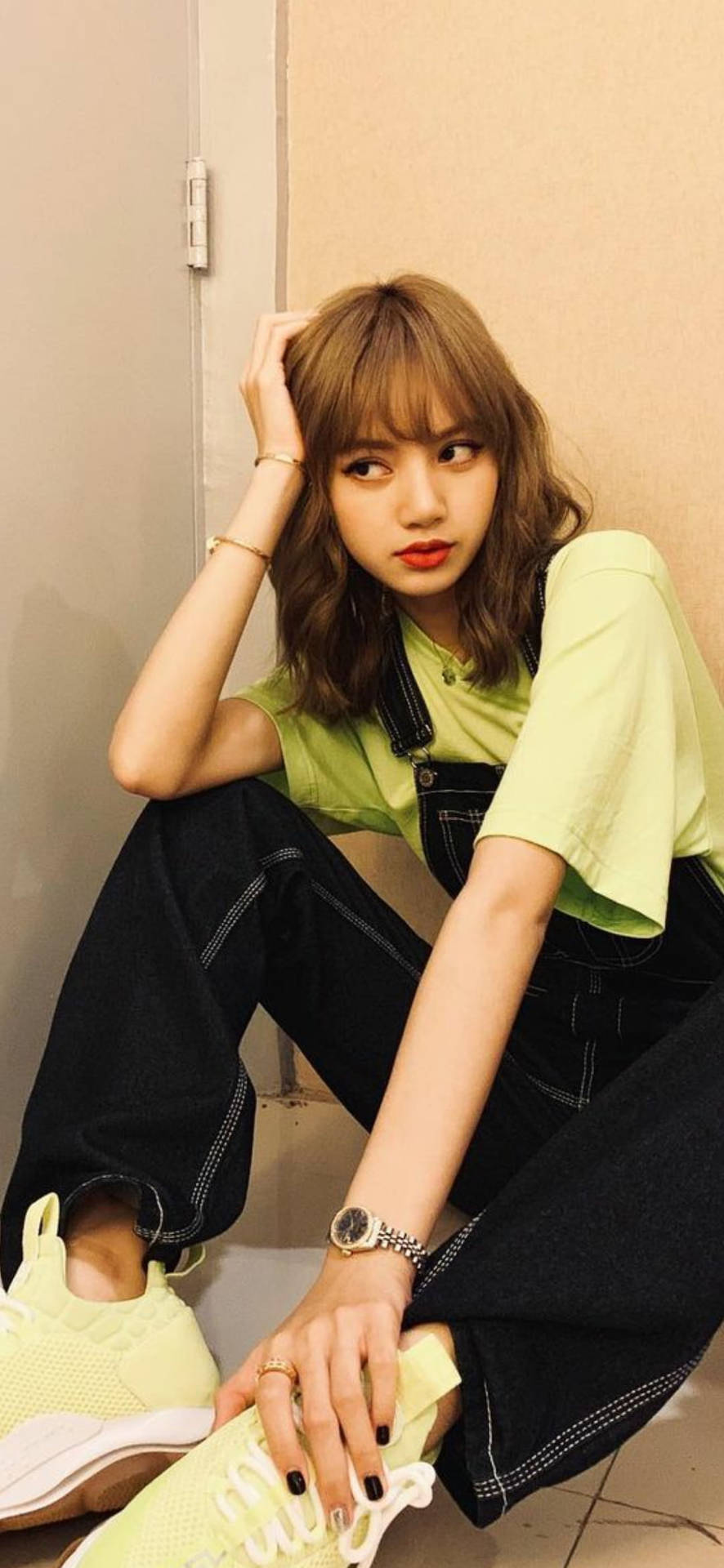 年輕女性身穿綠色襯衫和黑色吊帶褲，室內坐著，搭配運動鞋。 — Blackpink 壁紙