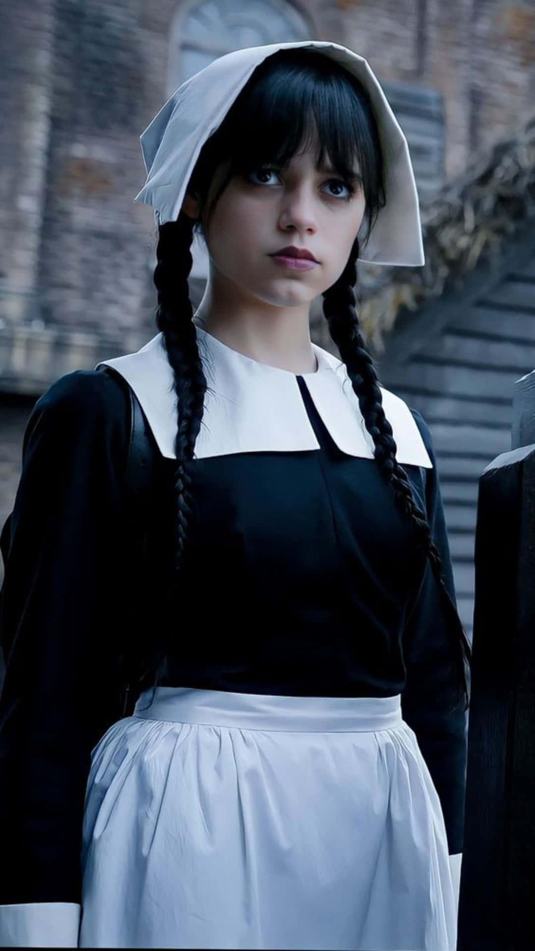  壁紙 — 一位年輕女子身穿黑白修女服，辮子頭髮，莊嚴地站在石建築背景前。