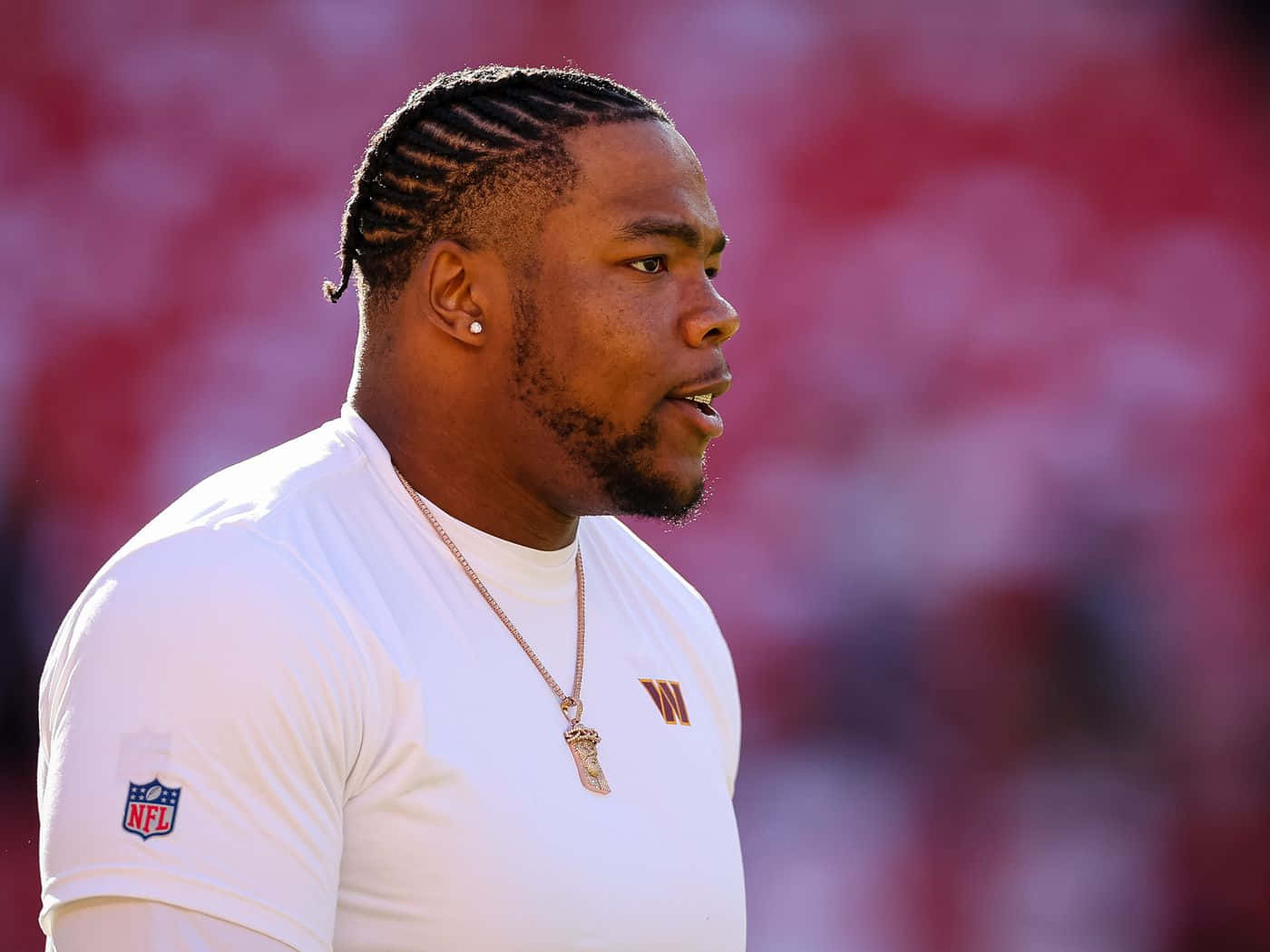  壁紙 — 一位身穿白色球衣、專注的NFL球員站在陽光明媚的球場上，身後是模糊的紅色體育場座位。