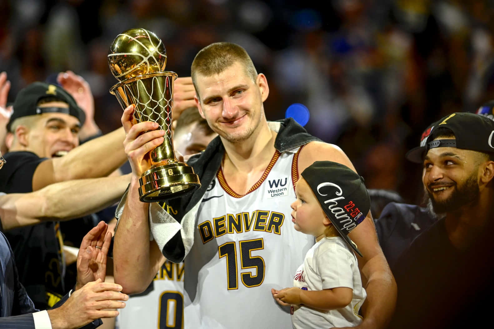 籃球運動員與戴著「Champ」帽子的孩子一起手持獎盃慶祝。 — NBA 壁紙