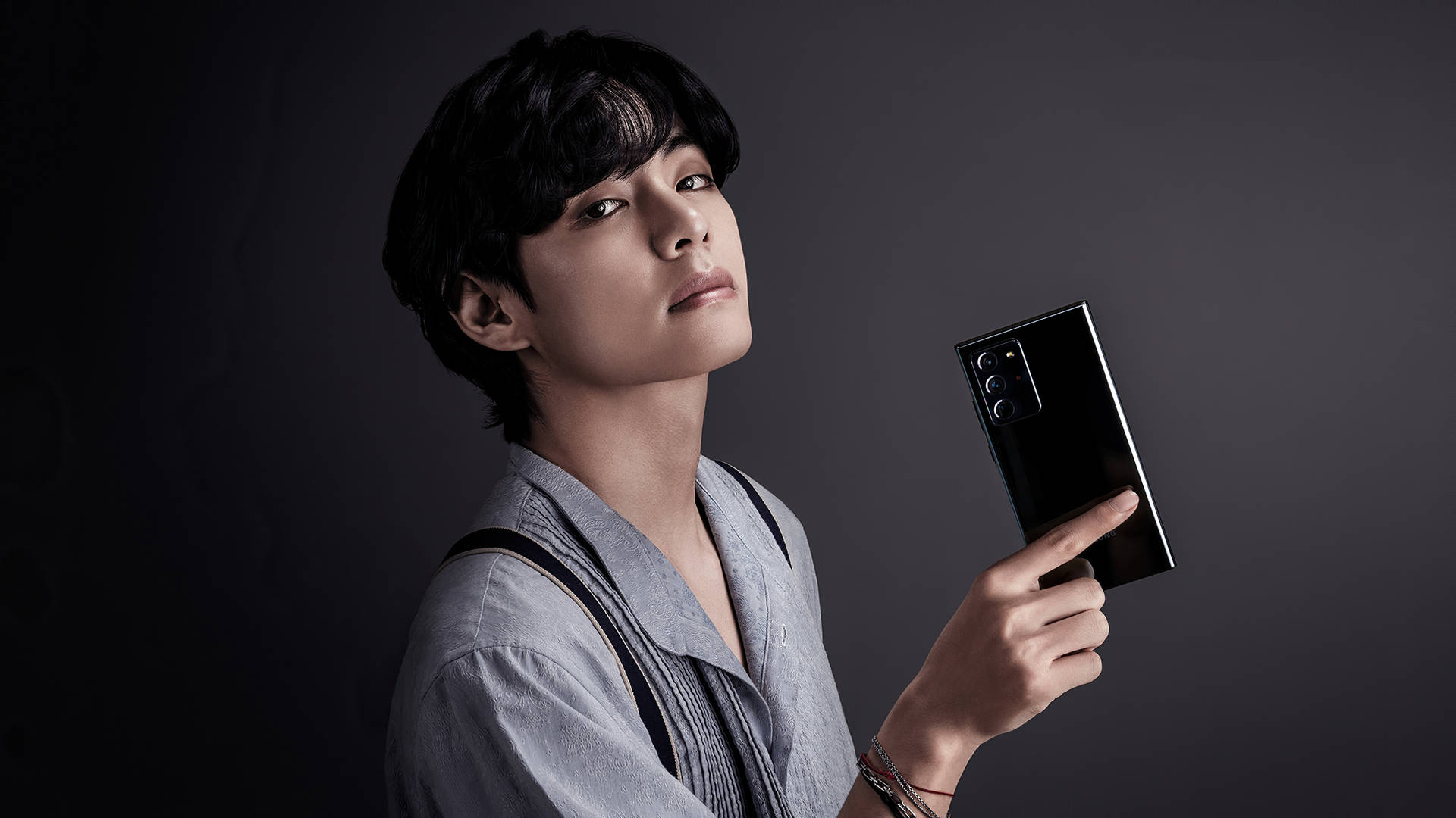 年輕男子在工作室中手持黑色智慧型手機 — K Pop 壁紙