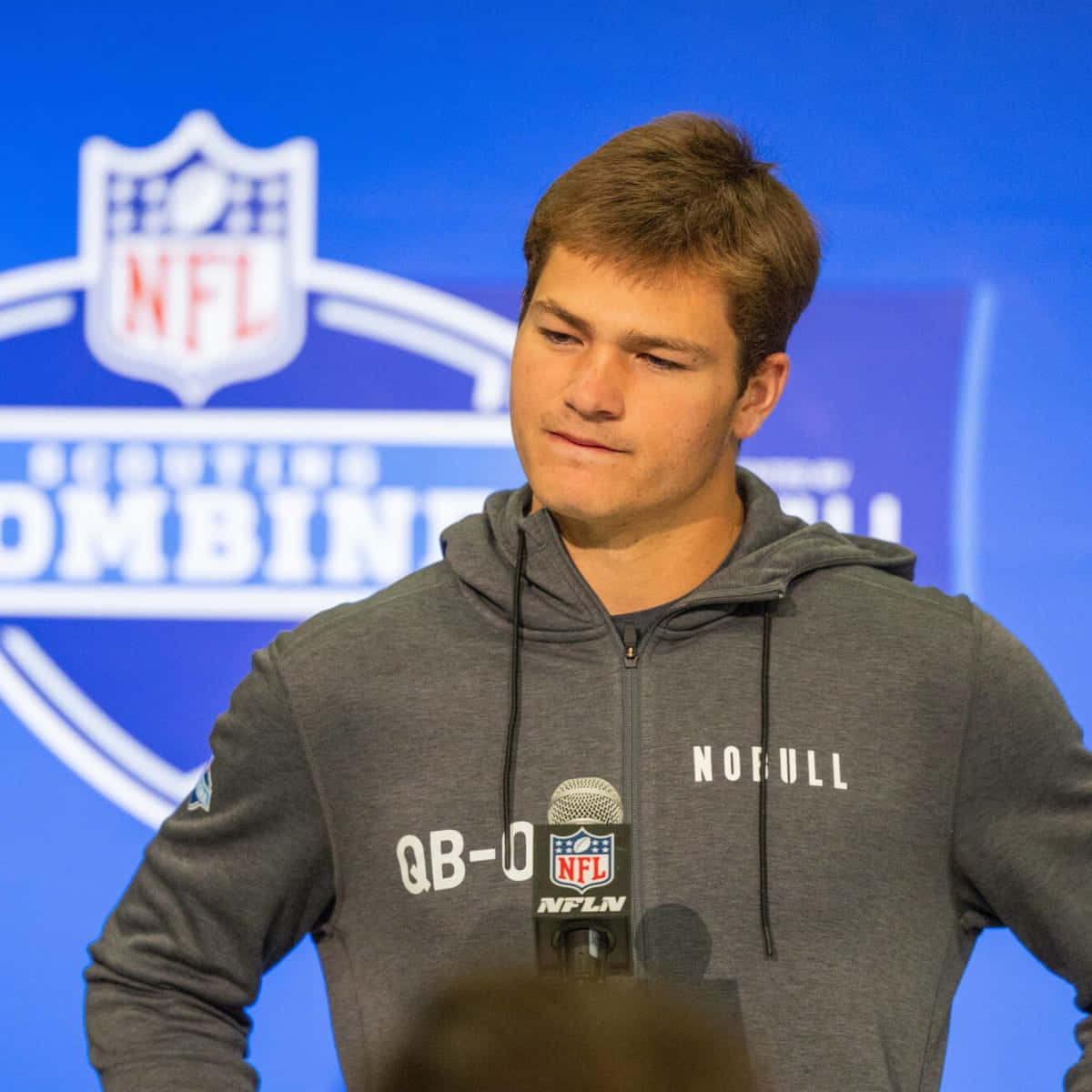  壁紙 — 一位身穿灰色連帽衫的年輕美式足球員在NFL選秀聯合試訓記者會上站在麥克風前。