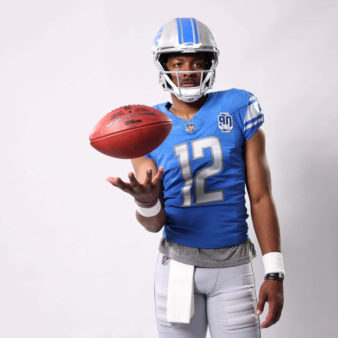  壁紙 — 一位身穿藍色12號球衣的底特律雄獅美式足球員，在純白色攝影棚背景前平衡一個紅色美式足球。