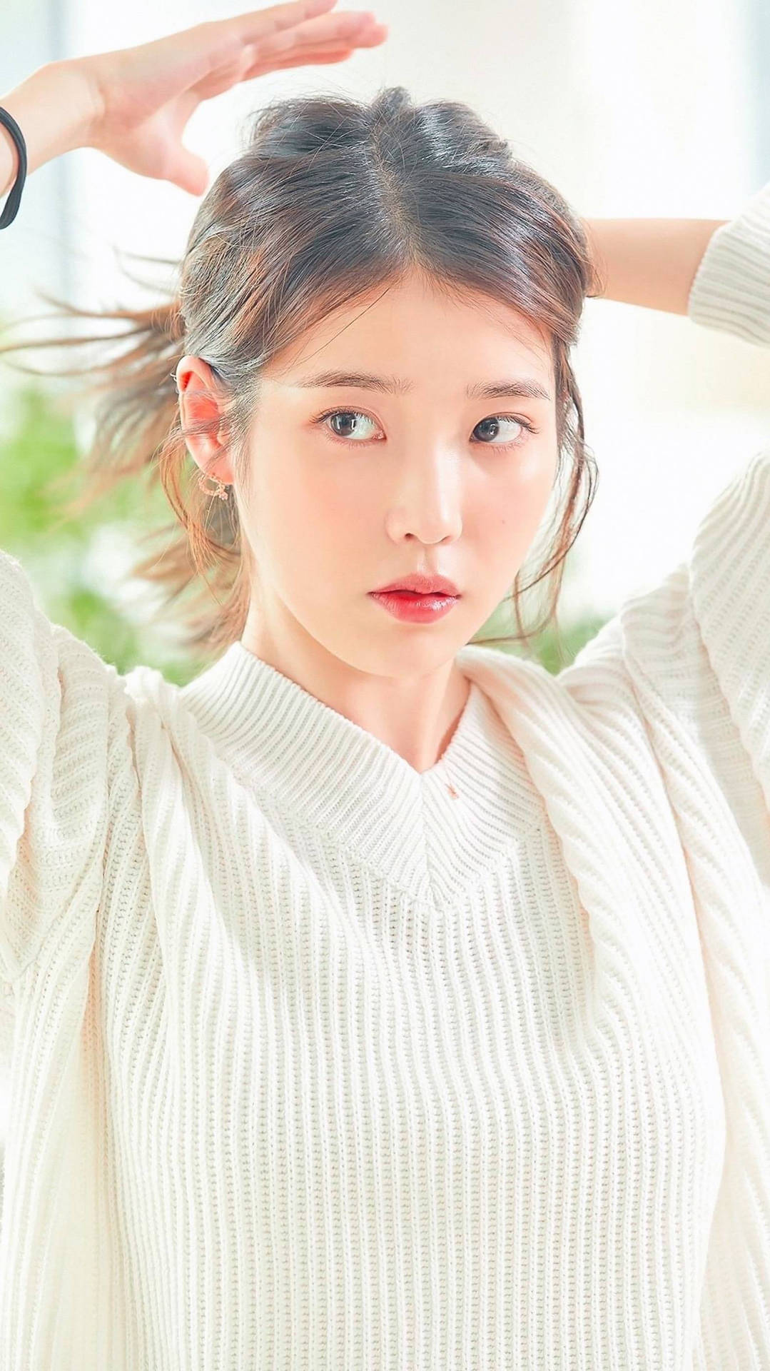 身穿奶油色毛衣的年輕女性在室內舉起雙手擺姿勢 — K Pop 壁紙