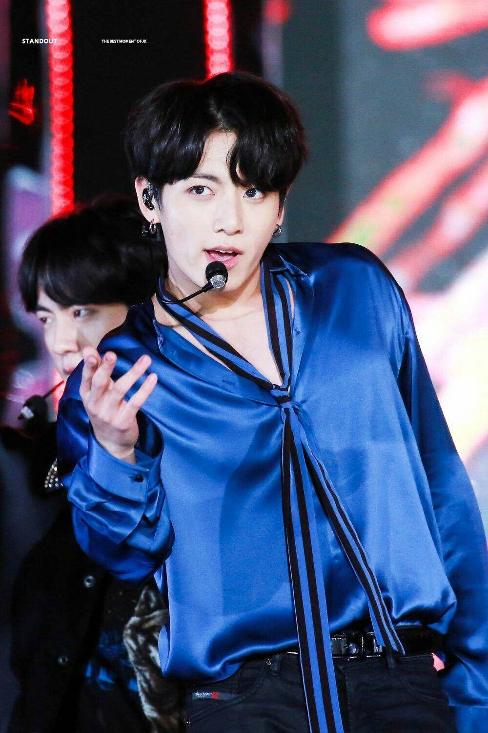 身穿藍色緞面襯衫的K-pop表演者在紅燈舞台上揮手。 — Bts 壁紙
