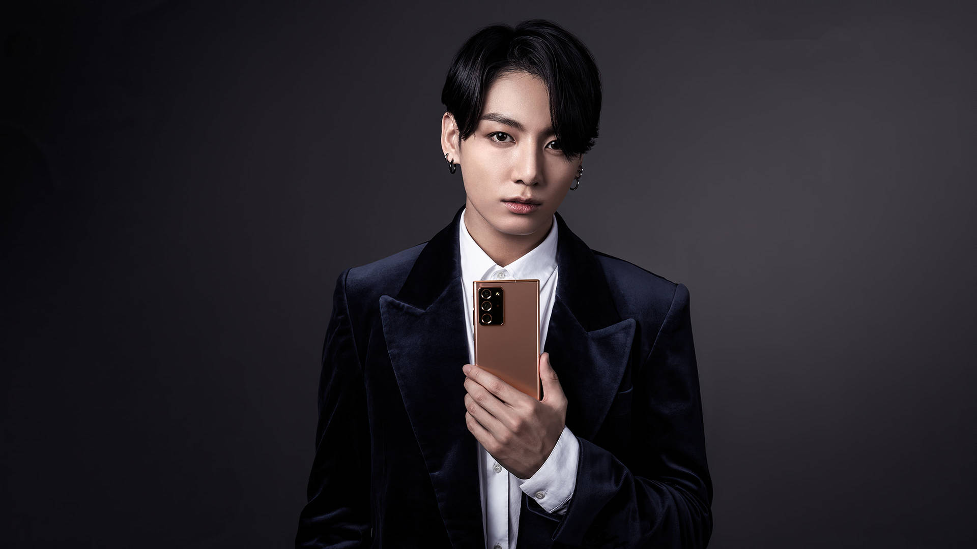 身穿天鵝絨西裝的男子在攝影棚中拿著玫瑰金智慧型手機 — Jungkook 壁紙