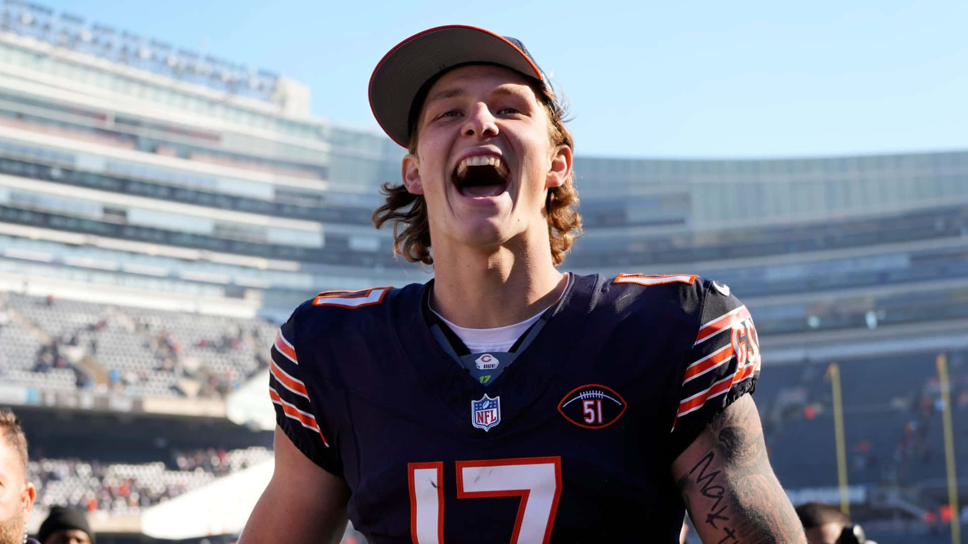  壁紙 — 一位身穿芝加哥熊隊球衣的NFL美式足球員在陽光明媚的球場上開懷大笑。