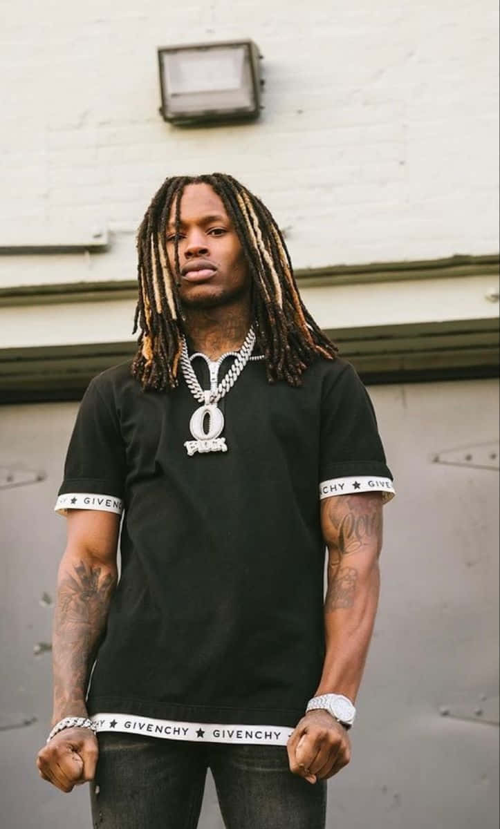 穿著街頭服飾、有刺青和鏈條項鍊的男士站在磚牆前。 — King Von 壁紙