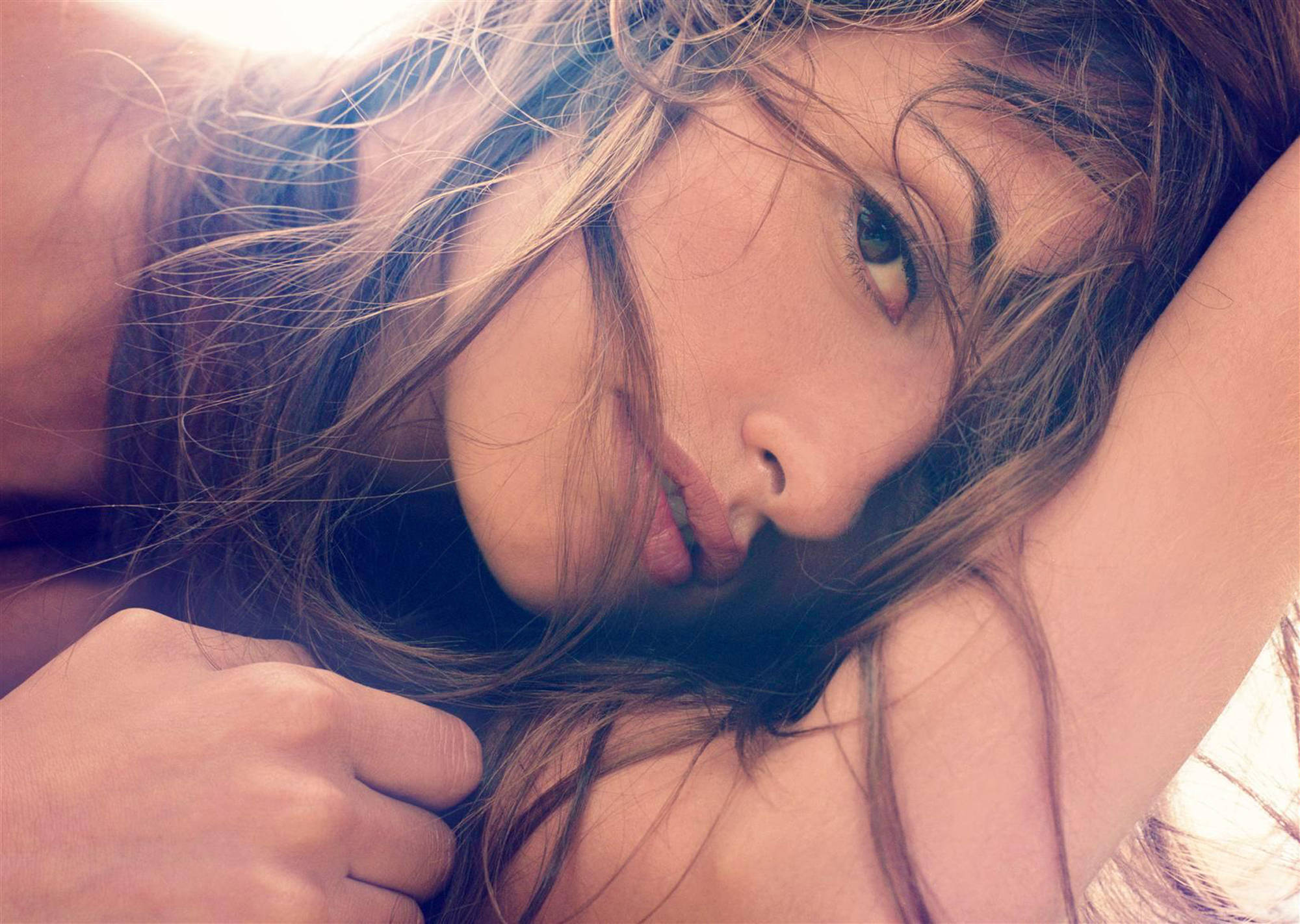 一位頭髮蓬鬆的女性將頭靠在手臂上，直視鏡頭。 — 4K 壁紙