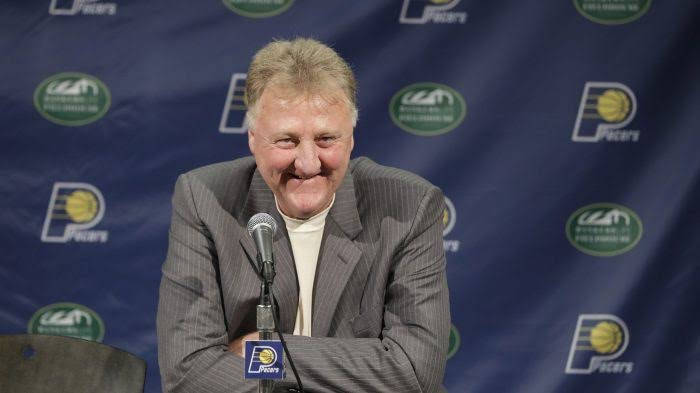 穿西裝的男子在記者會上微笑，背景有溜馬隊標誌。 — NBA 壁紙