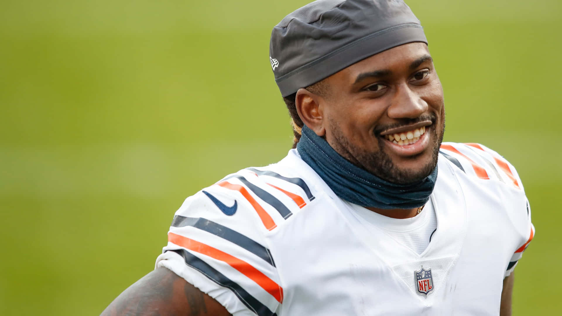  壁紙 — 一位微笑的NFL美式足球員，身穿芝加哥熊隊球衣和灰色頭帶，站在綠色球場上。