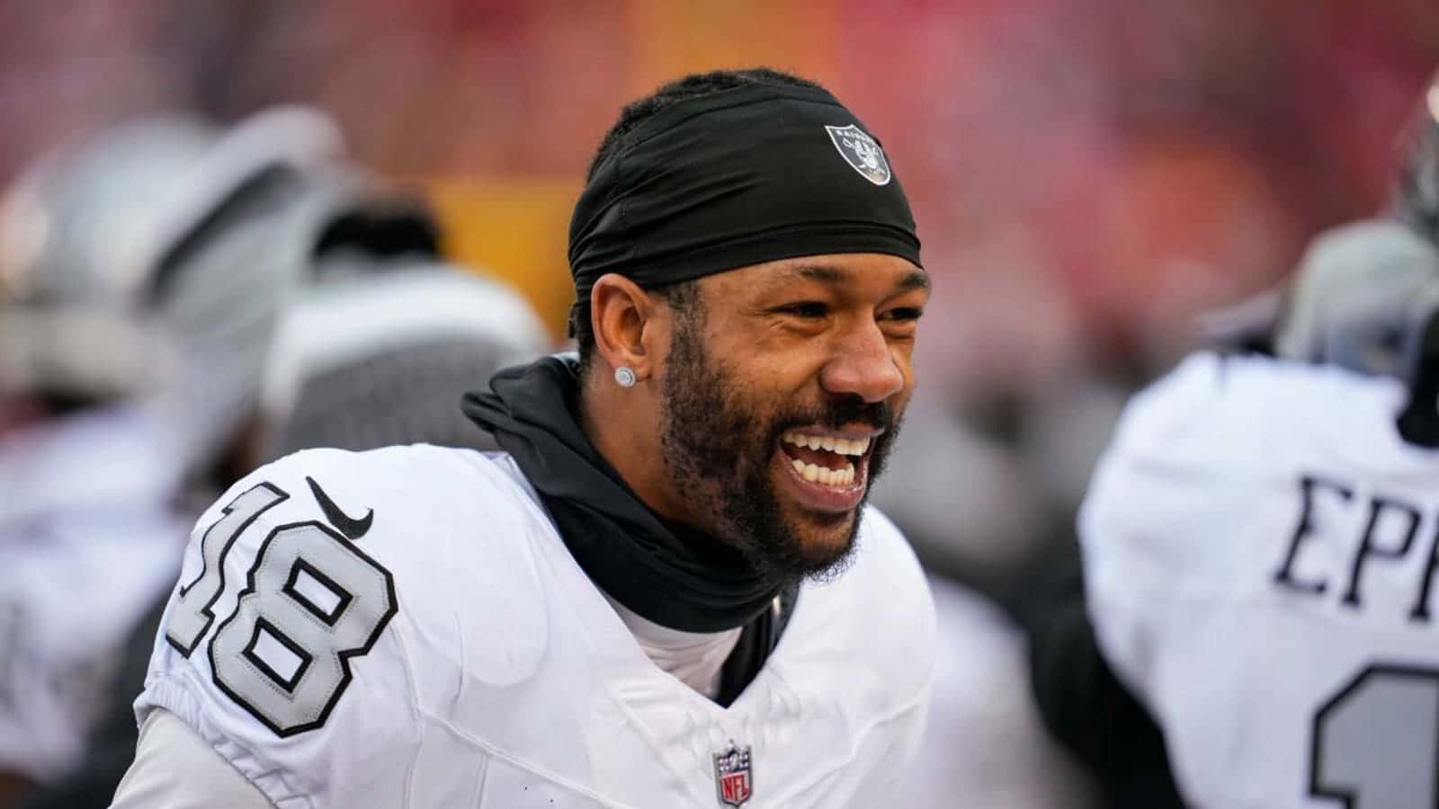  壁紙 — 一位微笑的NFL球員，身穿白色球衣，號碼18，戴著黑色頭帶，在模糊的球場上比賽時大笑。