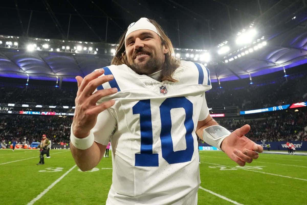  壁紙 — 一位微笑的NFL四分衛身穿白色10號球衣，在夜間燈火通明的體育場上慶祝。