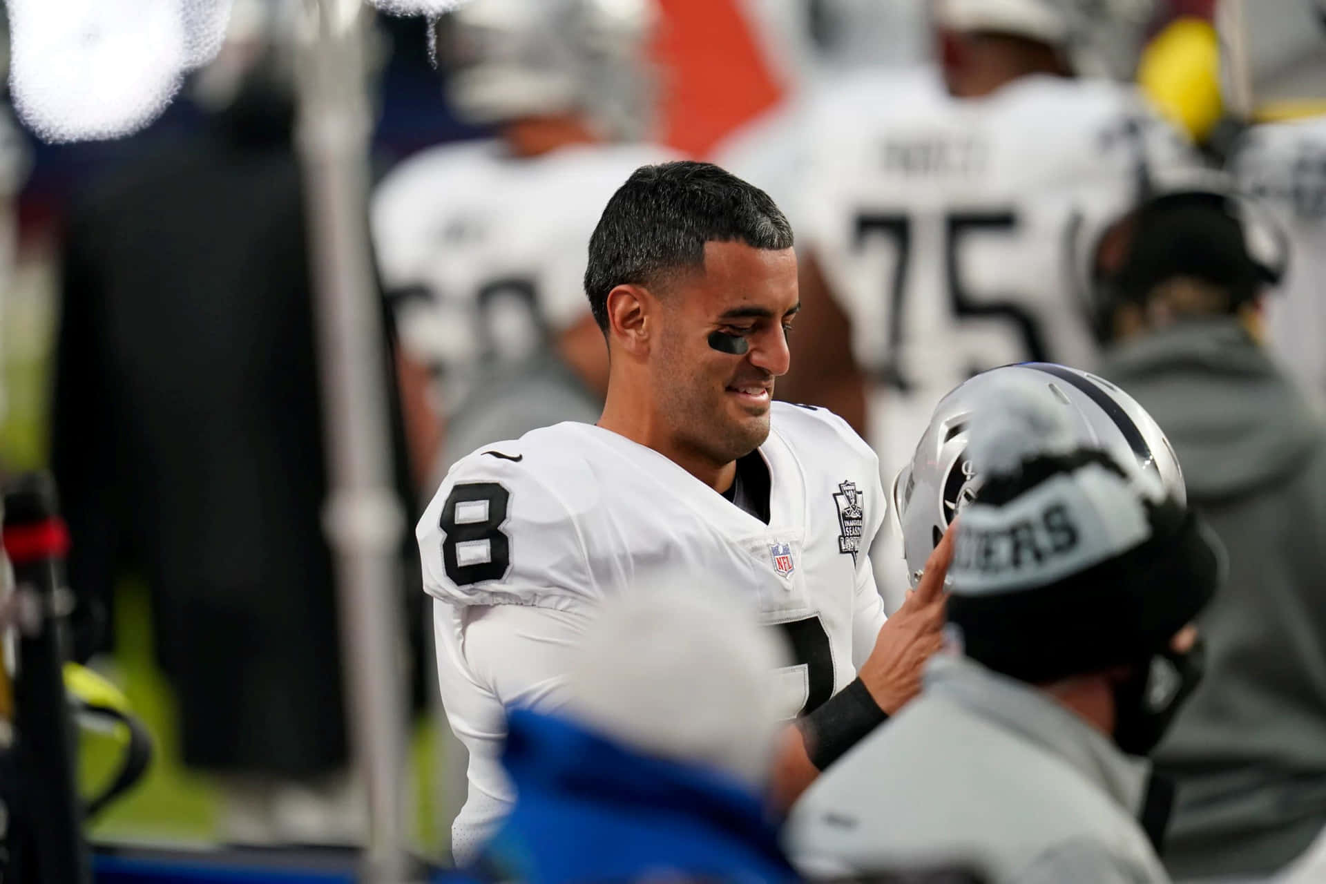  壁紙 — 一位微笑的NFL四分衛身穿白色8號球衣，在比賽期間與邊線上的隊友互動。