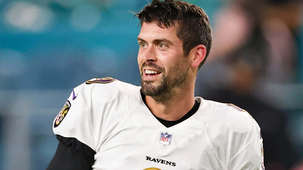  壁紙 — 一位微笑的NFL四分衛身穿白色烏鴉隊球衣，在球場燈光下的比賽中，專注地看向鏡頭外。
