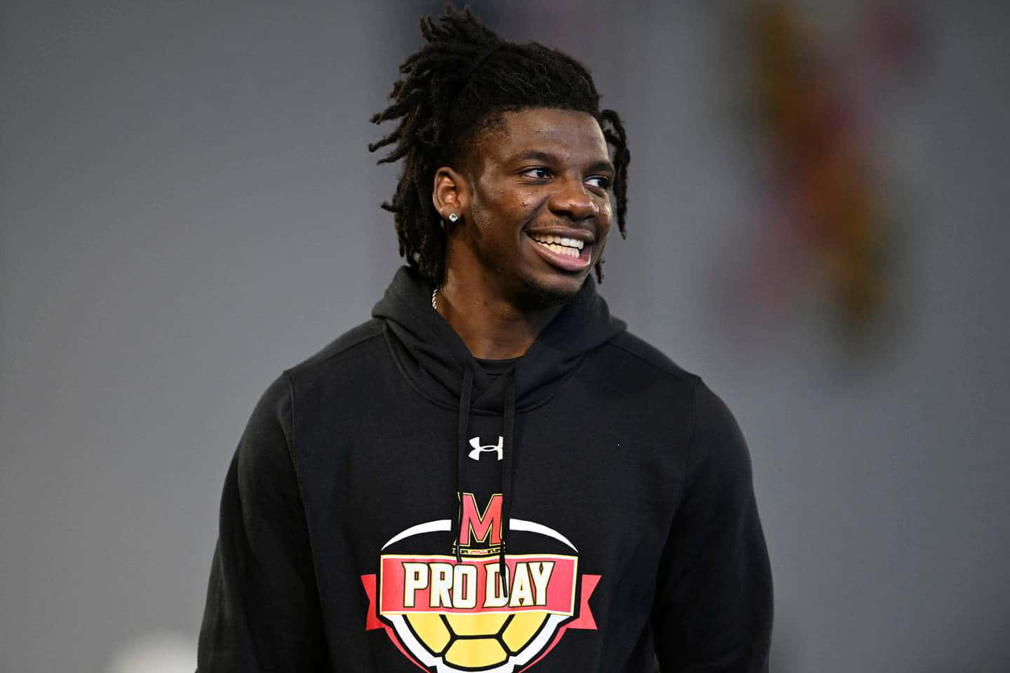  壁紙 — 一位微笑的年輕男子，留著辮子，穿著帶有'Pro Day'標誌的黑色連帽衫。