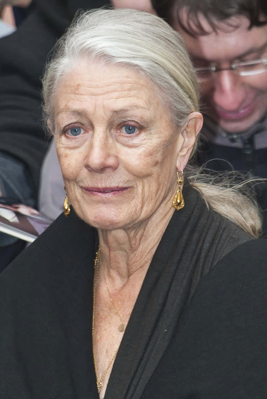 Vanessa Redgrave 桌布 壁紙 — 一位銀髮藍眼的老婦人戴著金飾和黑色上衣，正看著相機。
