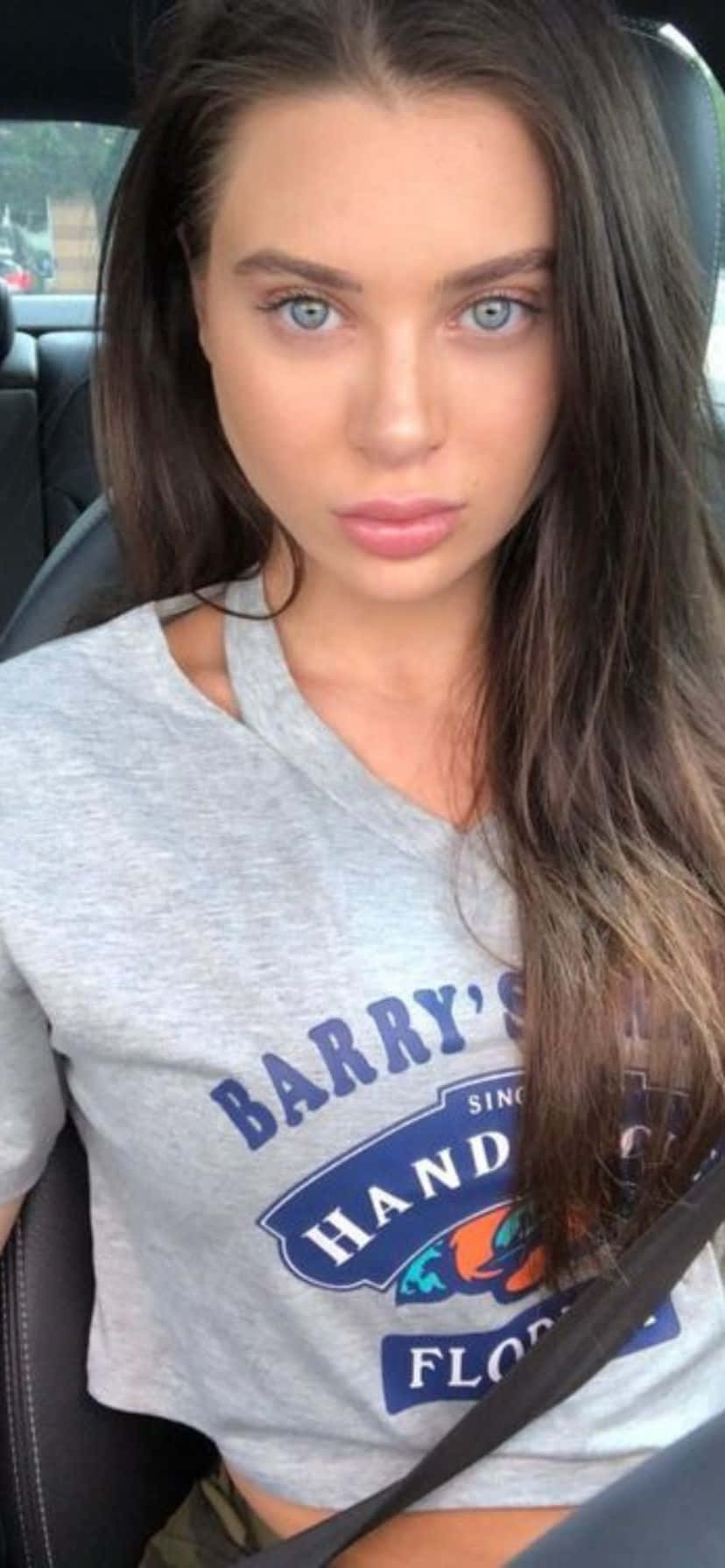  壁紙 — 一位擁有引人注目藍眼睛的年輕女性坐在車內，身穿灰色 'Barry's Hand Florida' T恤。