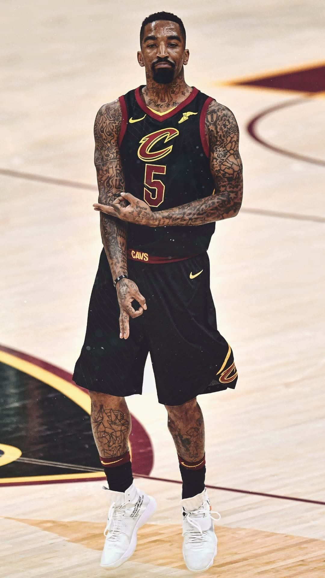  壁紙 — 一位有刺青的籃球運動員穿著黑色騎士隊球衣，雙手交叉，自信地站在硬木球場上。