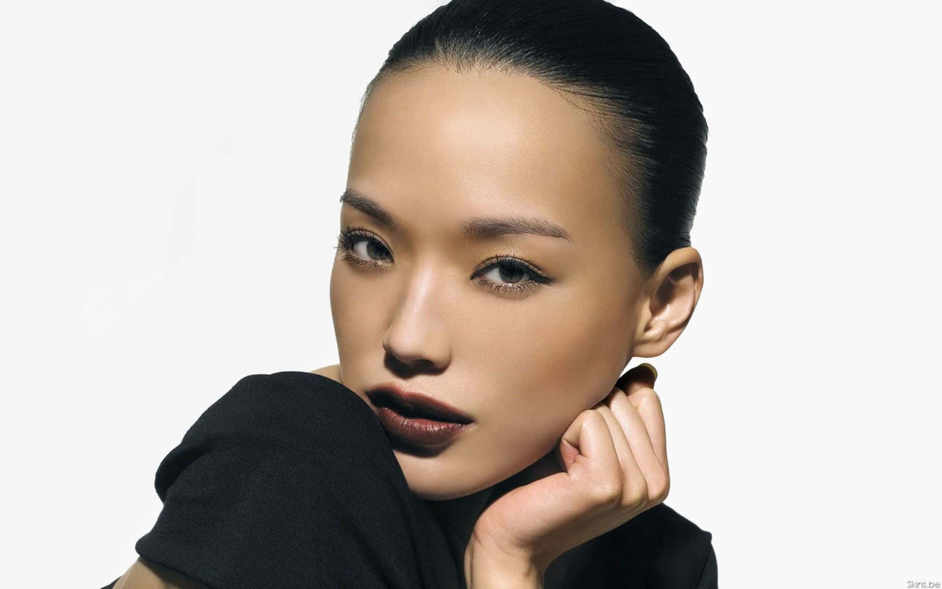 Shu Qi 桌布 壁紙 — 一位優雅的女人，擁有光滑的黑髮和鮮明的妝容，在純白背景上用手托著下巴。