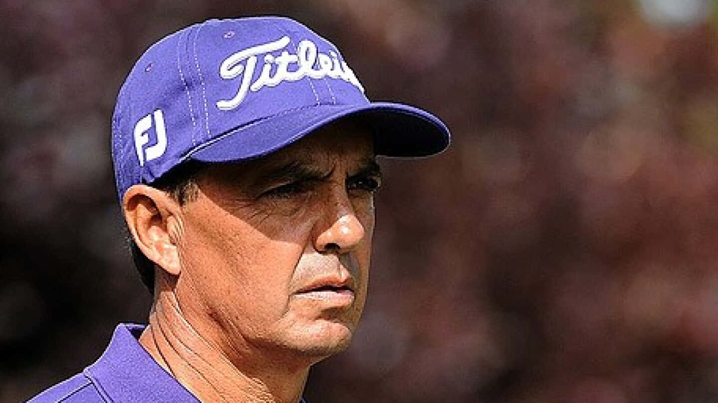  壁紙 — 一位專注的高爾夫球手戴著紫色Titleist帽子，在模糊的秋日背景下凝視著。