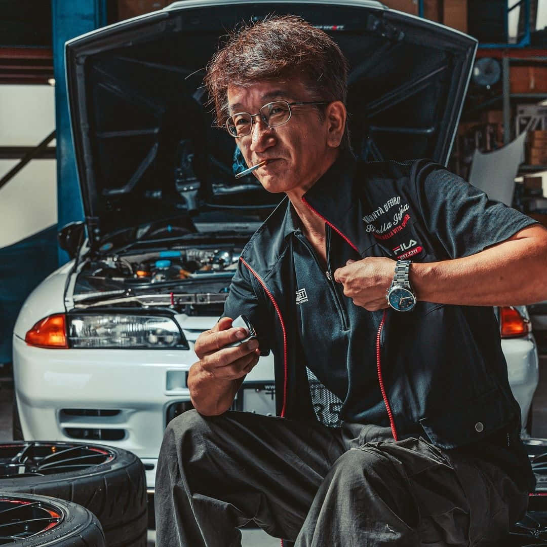  壁紙 — 一位專注的技師在車庫裡，坐在一輛引擎蓋打開的白色汽車前，手持工具。