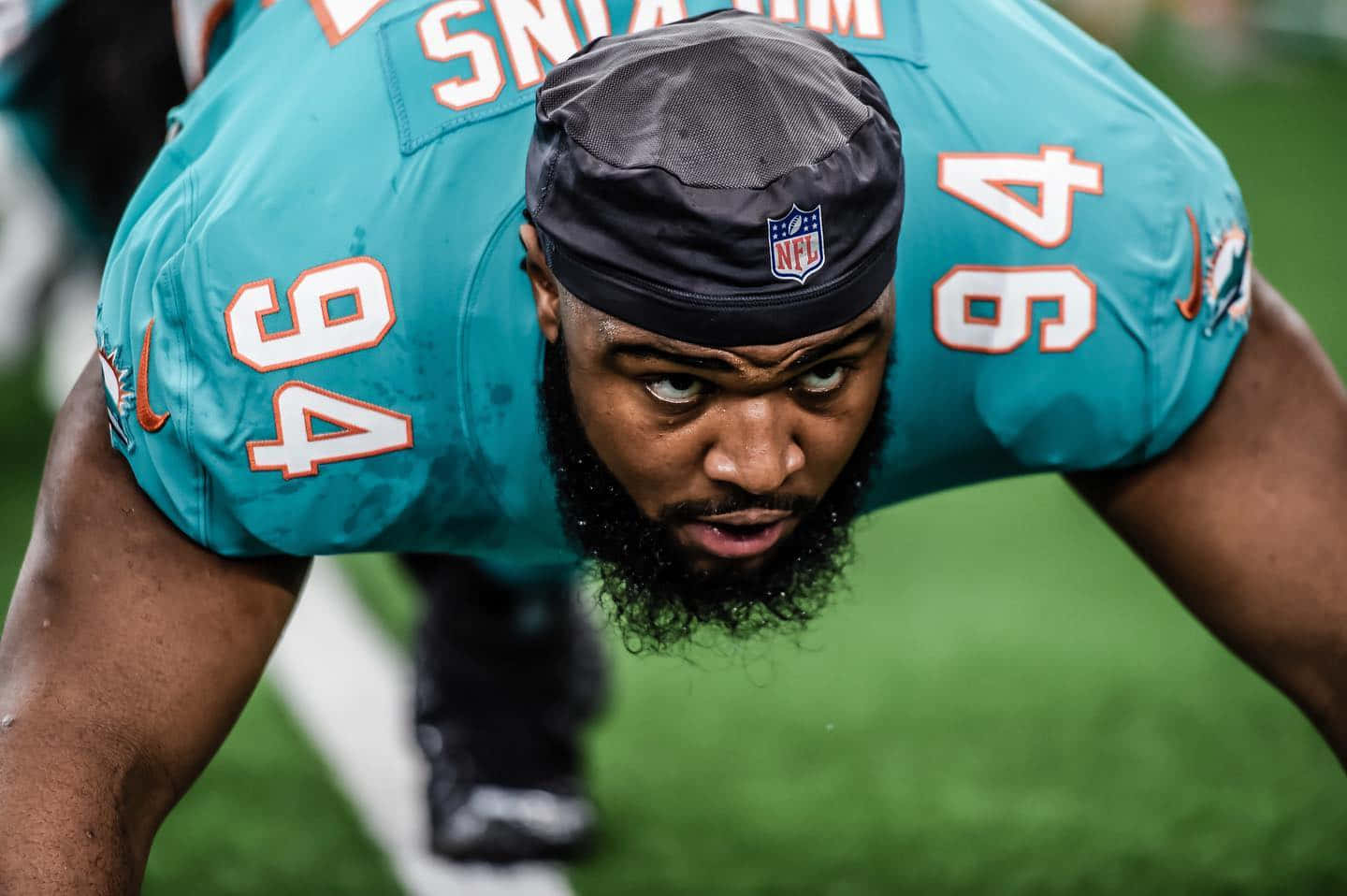  壁紙 — 一位專注的NFL防守端鋒，身穿青綠色94號球衣，在綠色球場上低蹲，充滿強烈決心。