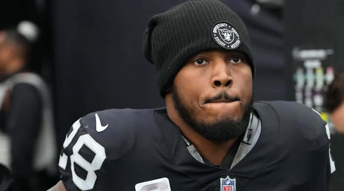  壁紙 — 一位專注的NFL美式足球員，身穿黑色Raiders球衣和毛帽，神情嚴肅地凝視前方。