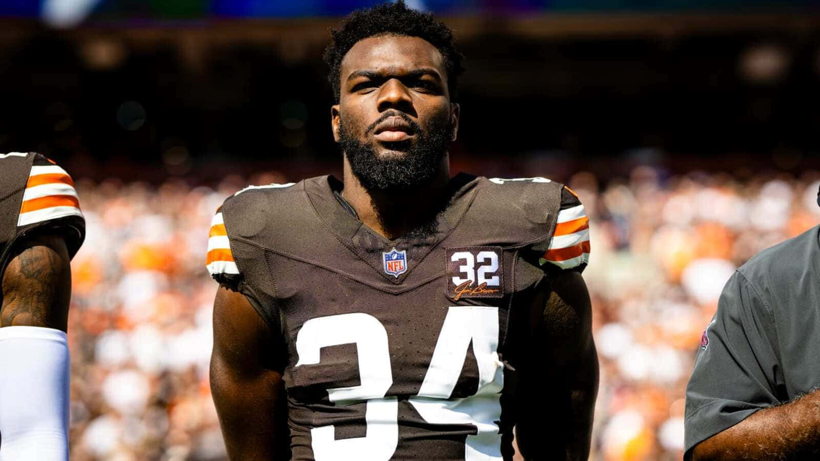  壁紙 — 一位專注的NFL美式足球員身穿棕色32號球衣，在明亮的體育場燈光下站在球場上。