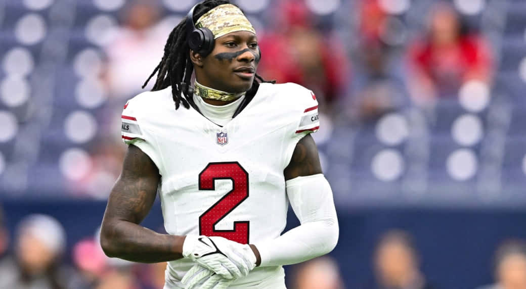  壁紙 — 一位專注的NFL球員身穿白色球衣，紅色號碼2，戴著耳機和頭帶站在體育場上。
