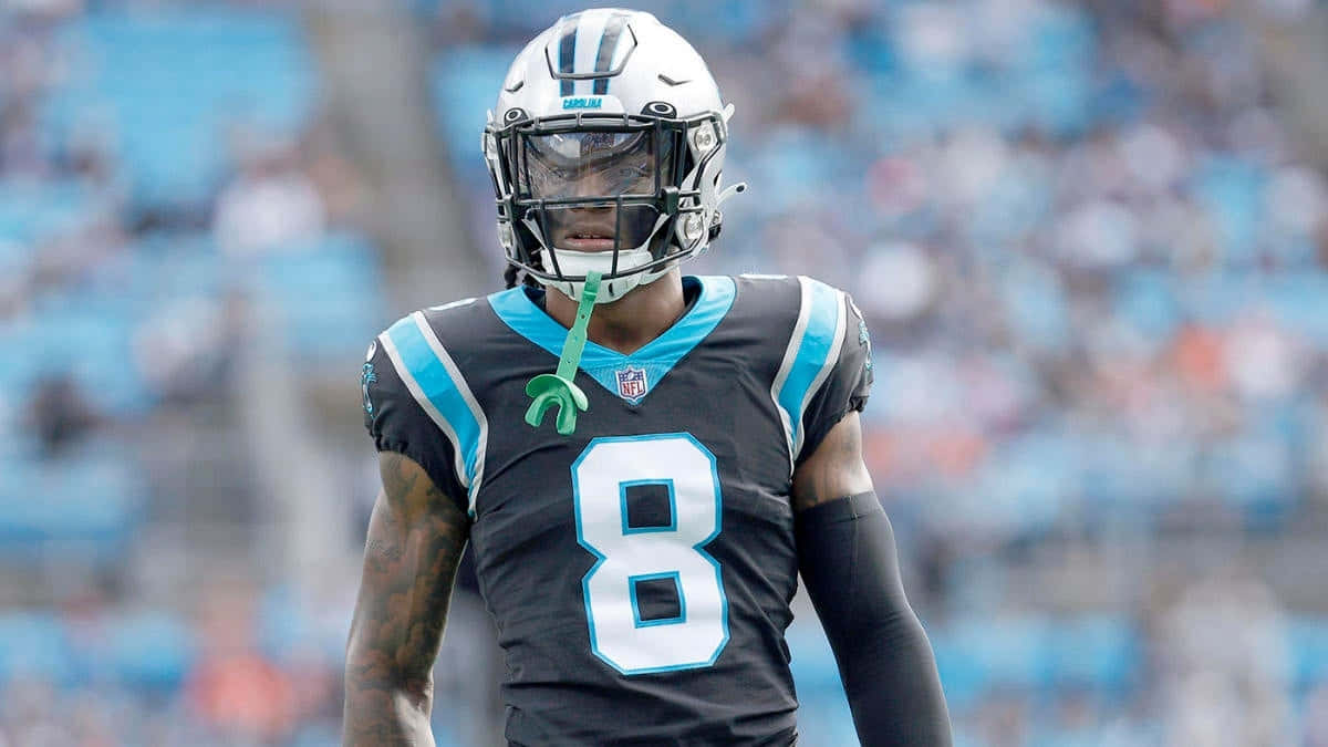  壁紙 — 一位專注的NFL球員身穿黑色和藍色球衣，號碼8，站在球場上，背景是模糊的體育場座位。