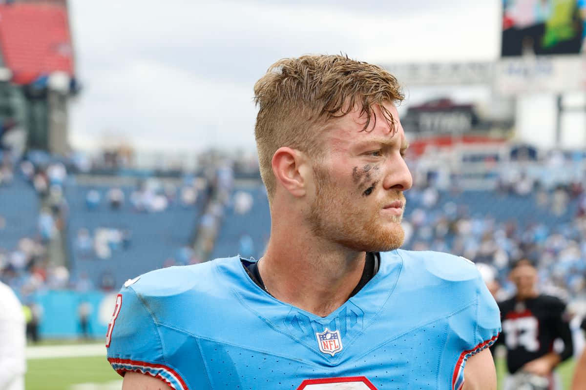  壁紙 — 一位專注的NFL球員身穿淺藍色球衣，站在體育場的場地上，背景是模糊的觀眾。