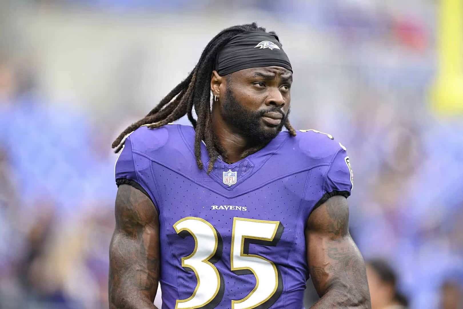  壁紙 — 一位專注的NFL球員身穿紫色烏鴉隊35號球衣，在日間比賽中站在球場上。