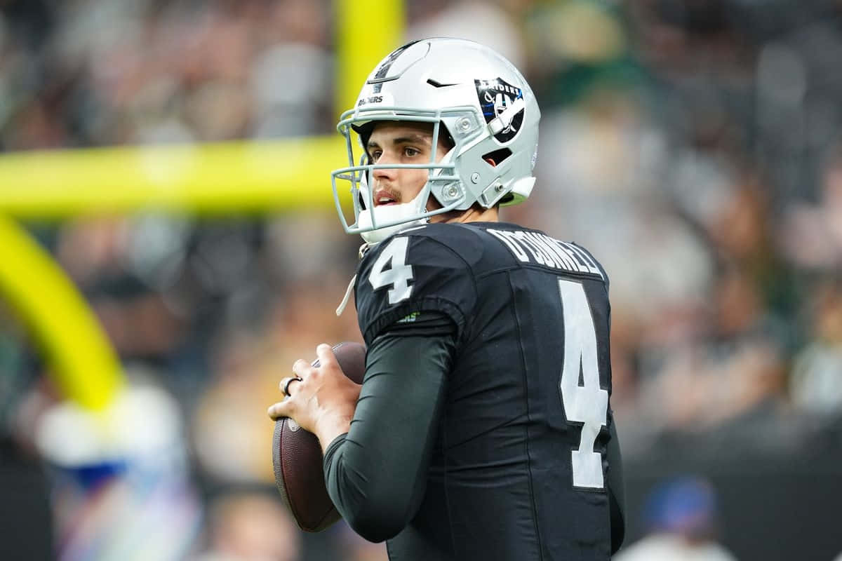 壁紙 — 一位專注的NFL四分衛穿著黑色和銀色制服，在比賽中拿著準備投擲的橄欖球。