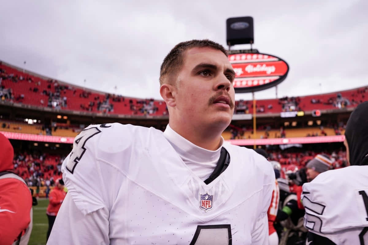  壁紙 — 一位專注的NFL四分衛穿著白色球衣站在球場上，背景有體育館人群和記分板。