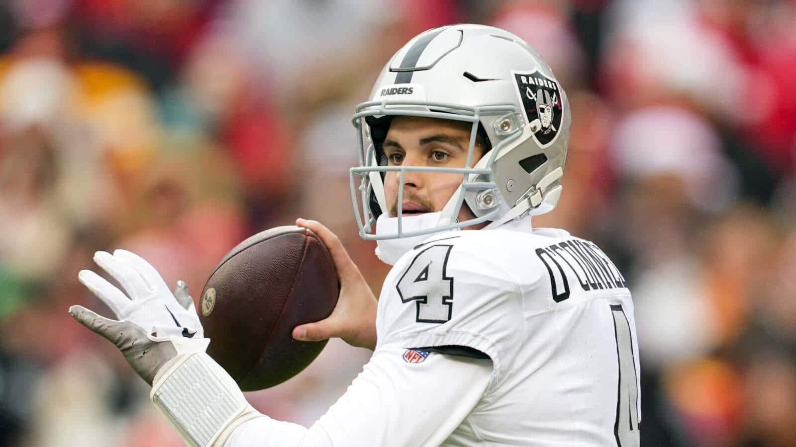  壁紙 — 一位專注的NFL四分衛穿著白色Raiders球衣，在日間比賽中準備投擲橄欖球。
