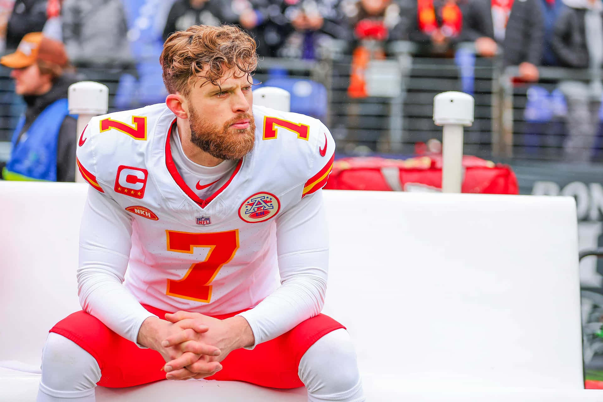  壁紙 — 一位專注的NFL四分衛身穿白色和紅色球衣，雙手交握坐在長凳上，在比賽中凝視遠方。