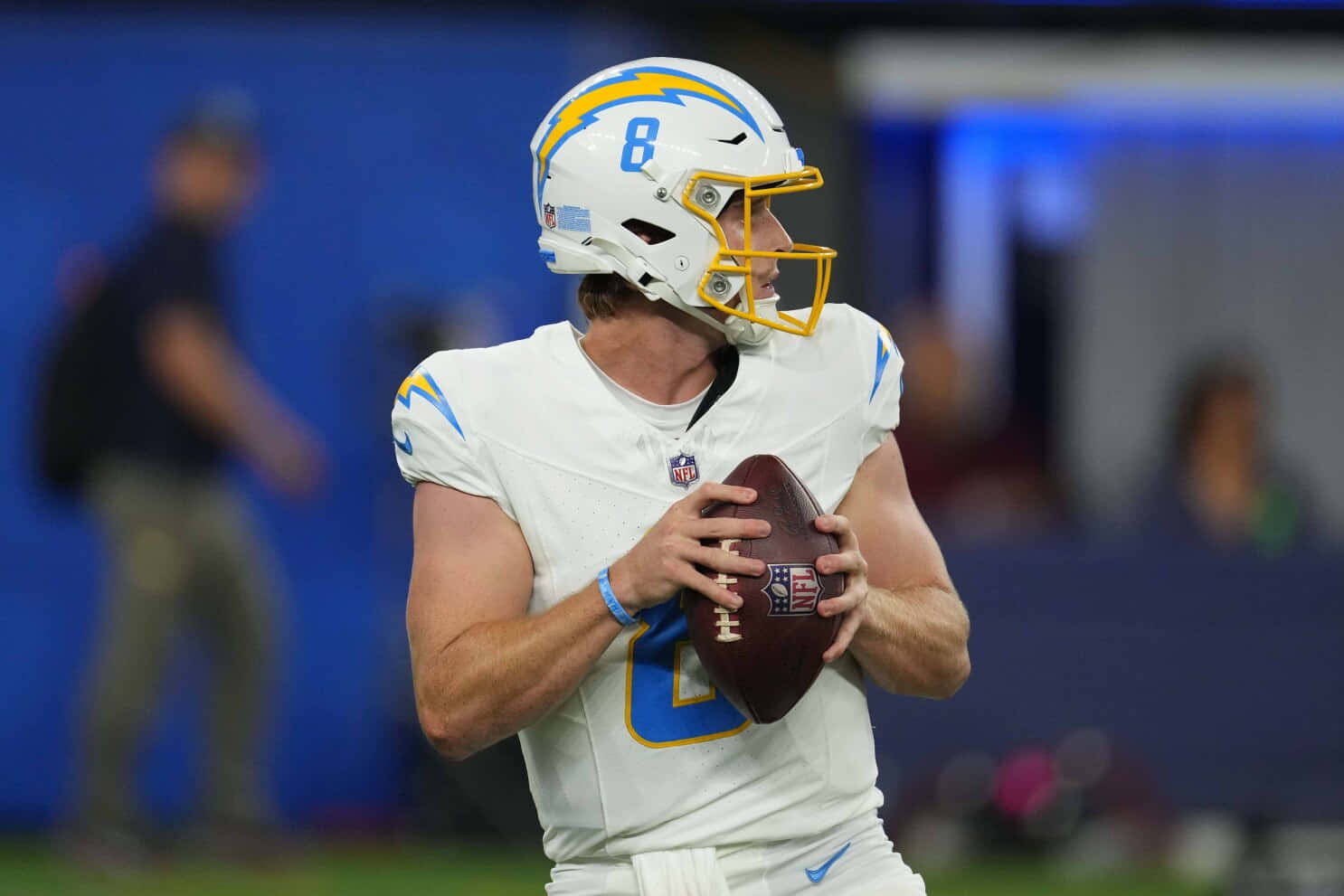  壁紙 — 一位專注的NFL四分衛身穿白色和藍色球衣，在球場燈光下的比賽中手持橄欖球準備傳球。