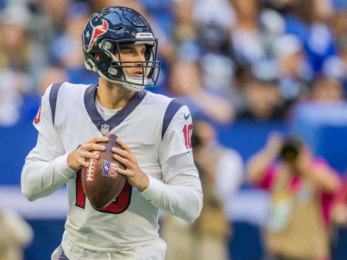  壁紙 — 一位專注的NFL四分衛身穿白色球衣，在日間比賽中手持橄欖球準備投擲，背景是模糊的體育場人群。