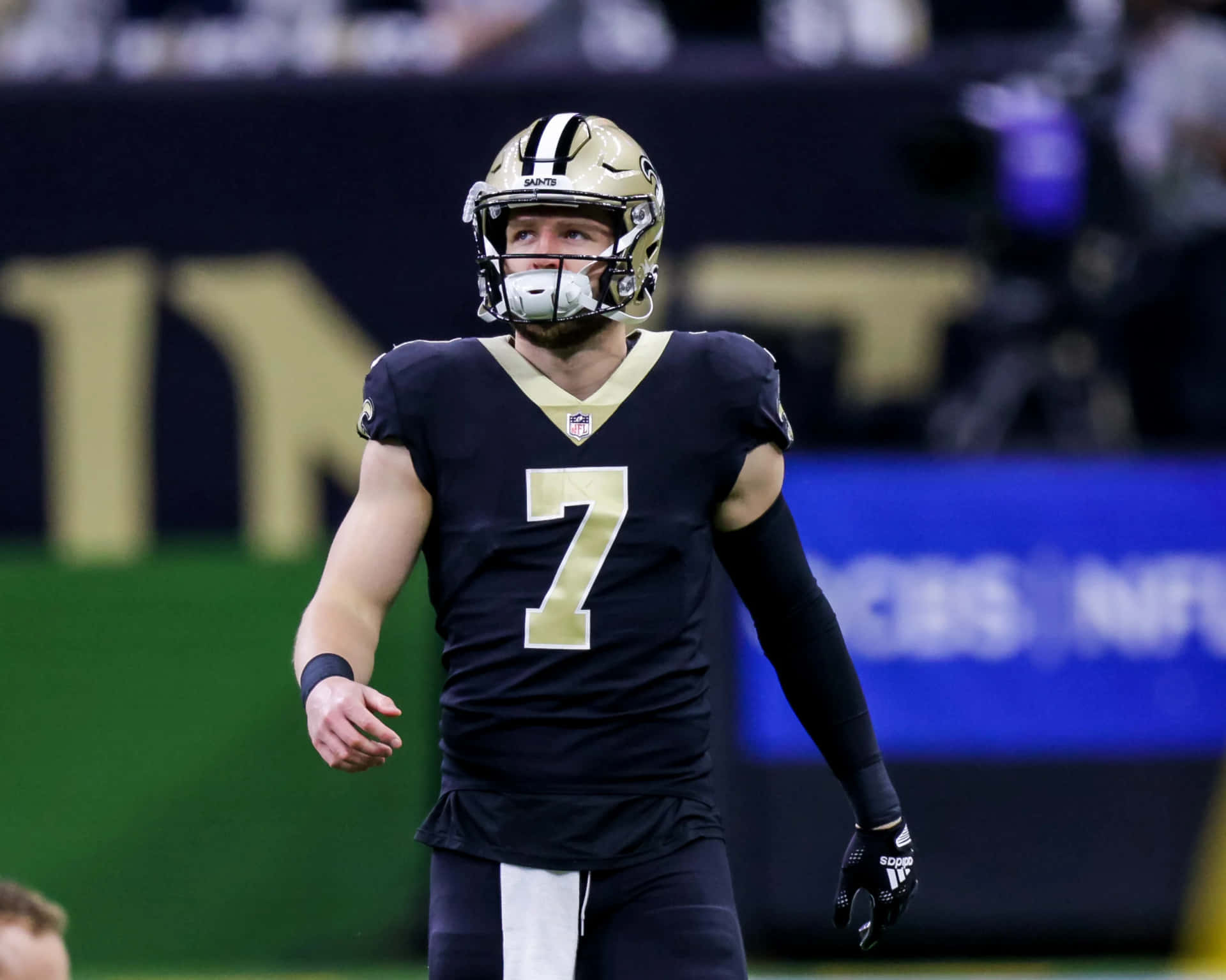  壁紙 — 一位專注的NFL四分衛，身穿黑金色7號球衣，在比賽中站在球場上。