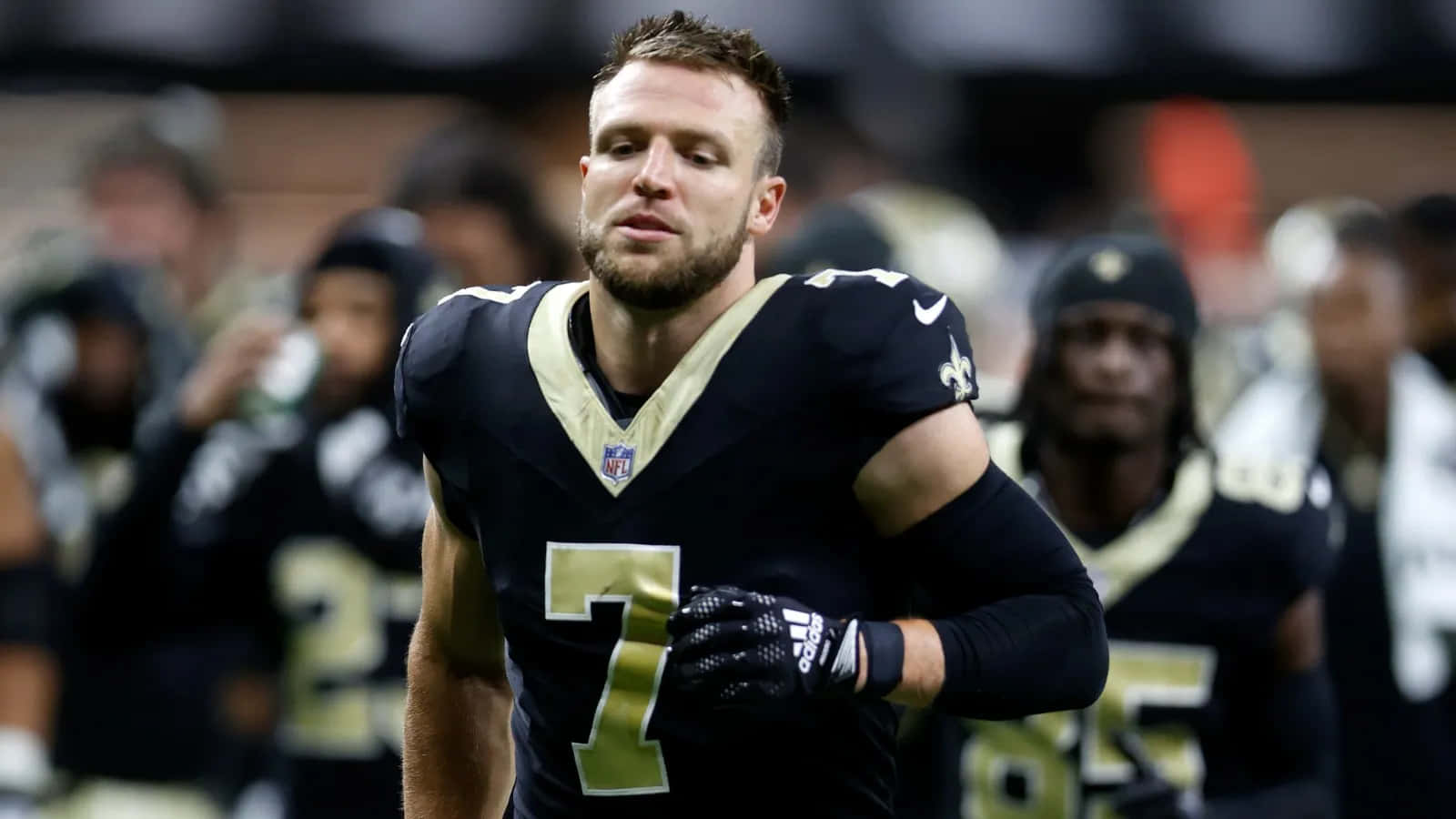  壁紙 — 一位專注的NFL四分衛身穿黑色和金色7號球衣在比賽中走進球場。