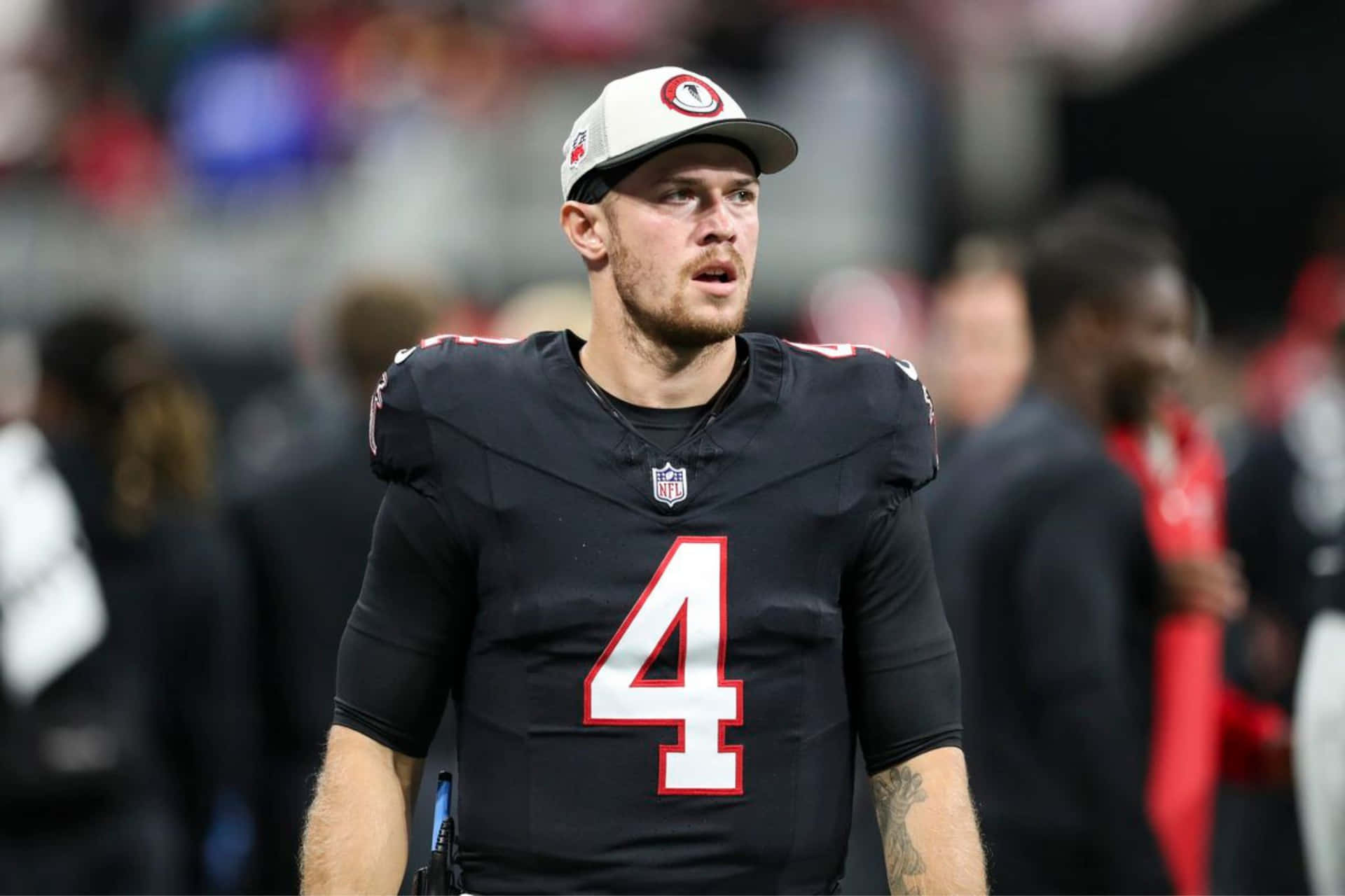  壁紙 — 一位專注的NFL四分衛身穿黑色四號球衣，在體育場燈光下於比賽中站在場上。