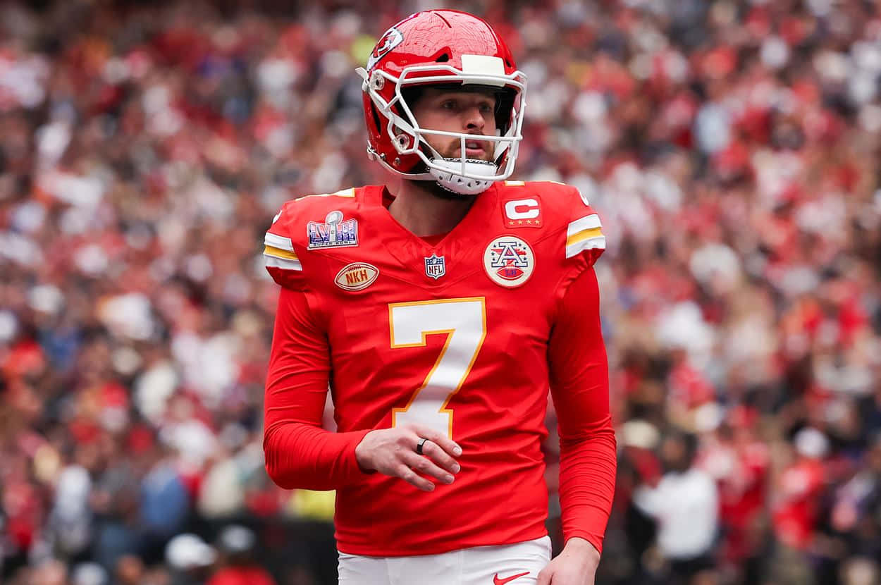  壁紙 — 一位專注的NFL四分衛身穿紅色7號球衣，在比賽中站在球場上，背景是模糊的人群。