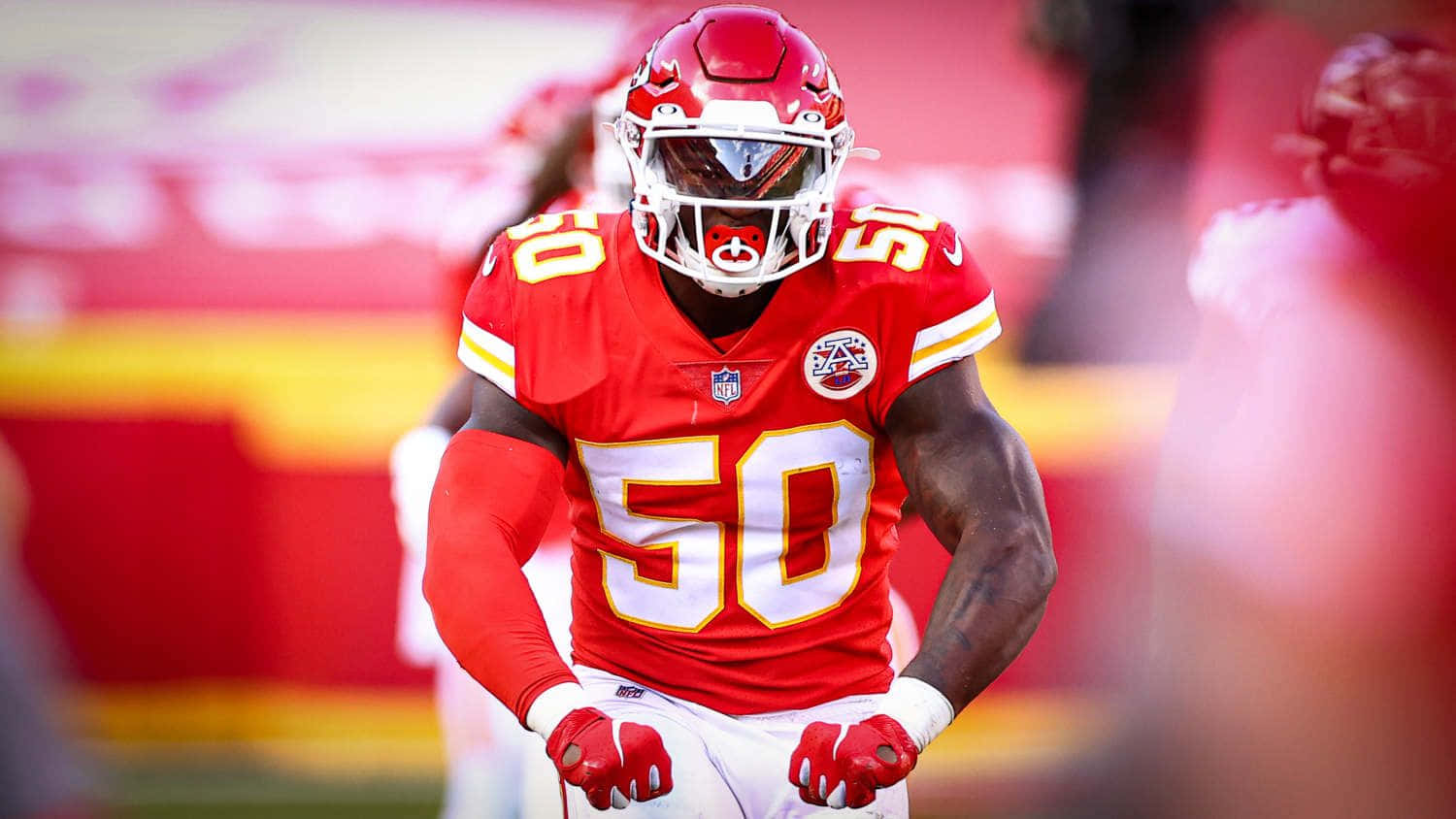  壁紙 — 一位專注的NFL線衛，身穿紅金色球衣，背號50，在比賽中準備就緒。