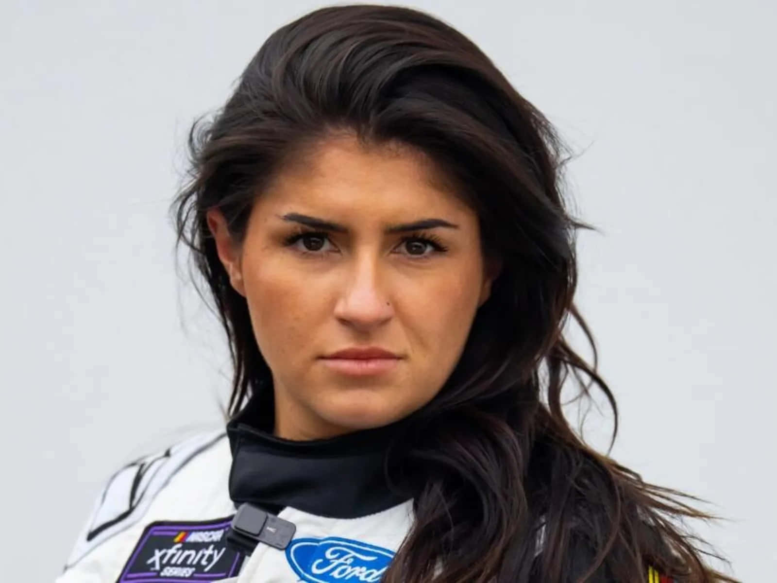  壁紙 — 一位專注的女性NASCAR Xfinity系列賽車手，身穿白色福特賽車服，深色頭髮微微飄動。
