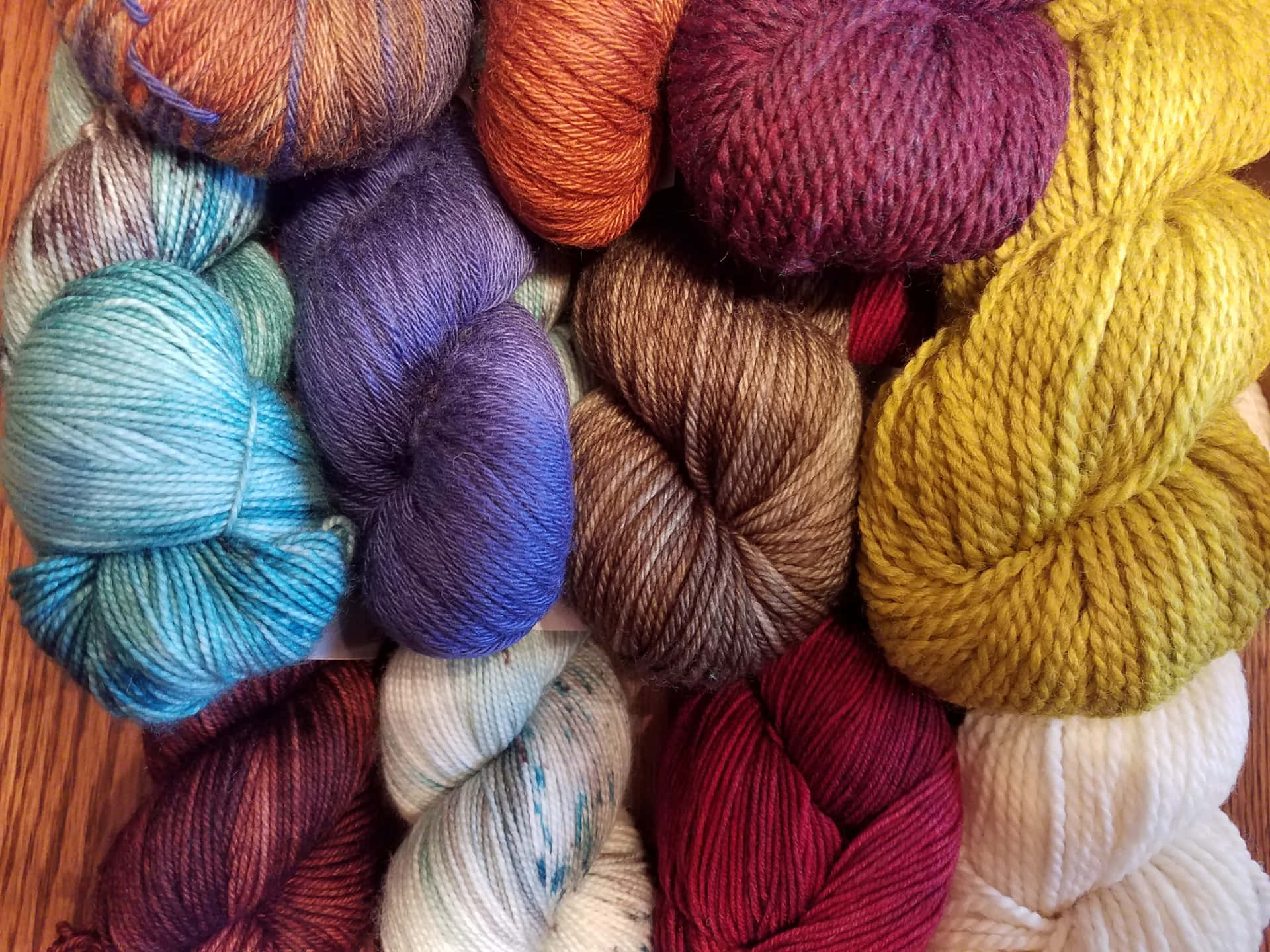 一束束色彩繽紛的手染紗線排列在木桌上。 — Stitch 壁紙