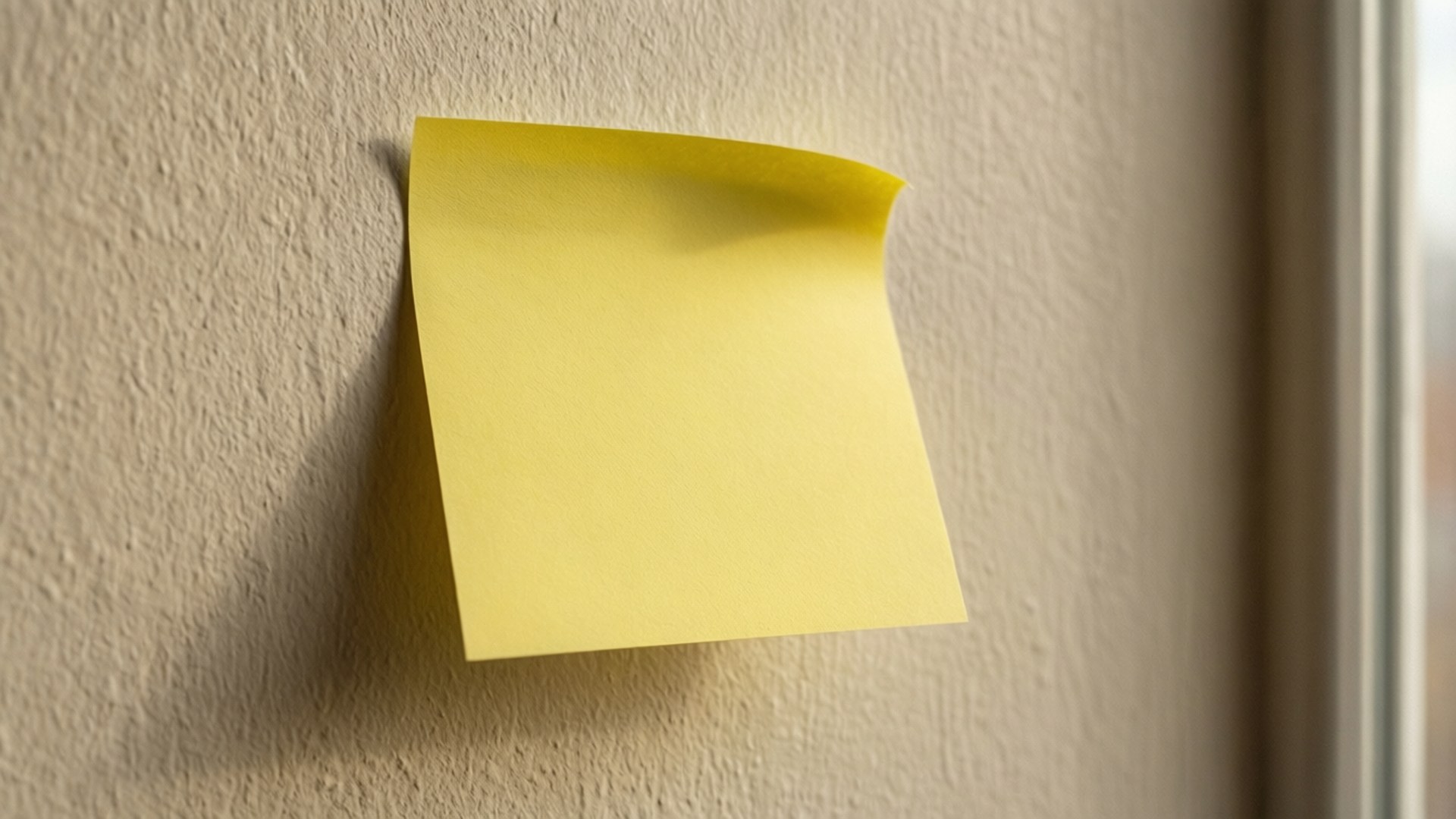 Post It 桌布 壁紙 — 一張黃色便利貼，角落微微翹起，貼在窗邊有紋理的米色牆上。